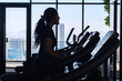 © Creativa Images - Silhouette of a woman exercising on a treadmill. A silhouette of a woman is exercising on a treadmill in a gym with large windows in the background showing a bright cityscape.