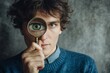© Rifqi - Young man holding a magnifying glass focusing on his eye against a grey backdrop, concept for investigation, vision enhancement and quality control