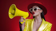 © JanSae Design - Stylish woman wearing a red hat, sunglasses, and a shiny yellow jacket holding a bright yellow megaphone against a vivid red background