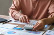 © Phimwilai - Businesswoman using calculator and analyzing financial charts at office desk