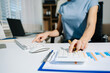 © Nuttapong punna - Women counting coins on calculator taking from the piggy bank. hand holding pen working on calculator to calculate on desk about cost at home office.