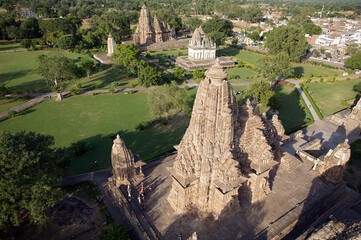 Aerial view of intricately carved sandstone temples pierce the sky amidst manicured lawns and scattered trees, echoing ancient artistry, Khajuraho, Madhya Pradesh, India.