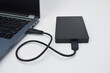 © Maule - External hard drive connected to laptop with USB cable on white desk, concept of portable storage, data transfer, and backup technology.