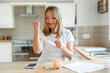 © Iryna - Woman celebrates financial achievement in a bright kitchen while focused on her budgeting efforts and saving goals