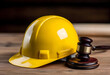 © sornram - A close-up view of a yellow hard hat positioned next to a wooden gavel, symbolizing safety and legal aspects in the construction industry.