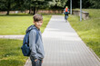 © Emvats - Boy in a gray hoodie with a blue backpack stands on a paved pathway, hands in pockets, looking to the side with a slight smile.