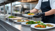 © Cam - canteen worker serving food on plate from buffet person wearing black gloves cook in white shirt dark apron serving meal in cafeteria variety of dishes on display food preparation catering