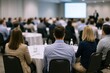 © The Little Hut - Business Conference Attendees Listening to Speaker Presentation in Large Hall with Projector Screen