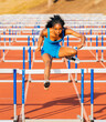 © Connect Images - Athlete in blue jumpsuit clears hurdle on outdoor track with determination and focus. USA
