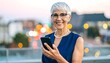 © art - A smiling mature woman in a blue business suit uses her smart phone outdoors in the evening light.