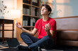 © PaeGAG - Teenage boy meditating on yoga mat, practicing mindfulness and finding inner calm in sunlit living room