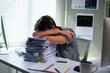 © PaeGAG - Exhausted office worker resting his head on a large pile of paperwork, overwhelmed by workload and deadlines
