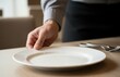 © Vadym - Neat uniformed waiter placing plate gently on simple tidy table in minimal uncluttered scene showing professional respect and balanced attitude to service