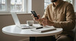 © Mono - A man works on his laptop and cellphone at a table in a modern office.