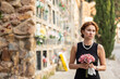 © JackF - Elegant grieving woman in forties, wearing formal black dress and pearls, standing with bouquet in hands near stone columbarium wall in cemetery, gazing sorrowfully and contemplating loss
