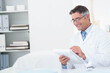 © WavebreakMediaMicro - Mature doctor in lab coat reviewing clipboard paperwork at office desk with spine model, copy space