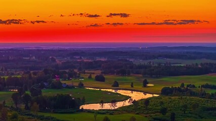 Wall Mural - Sunset over patchwork farmland and winding country roads with warm orange reds reflected in water