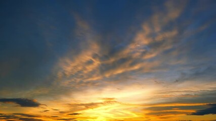 Wall Mural - A sunset time-lapse captures fiery orange and gold clouds spreading across a deep blue sky, blending into soft purples, reflecting the shifting moods of evening weather and nature’s dramatic display.
