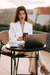 © Darius - Business professional working on laptop outdoors in stylish attire during sunset