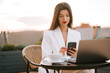 © Darius - Professional woman working on a laptop outdoors with a smartphone at sunset
