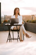 © Darius - Professional woman working on laptop outdoors at sunset in a serene rooftop setting