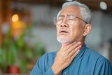 An elderly man with glasses holds his throat in pain, showing discomfort or a sore throat, possibly indicating illness or difficulty swallowing