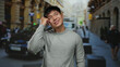 © Krakenimages.com - Young chinese man in gray sweater having a bright idea on a city street with taxis and people in the background, suggesting a lively urban environment.