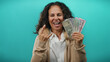 © Krakenimages.com - Middle-aged woman holds indian rupees with a rock gesture on an isolated blue background, showcasing money and excitement.
