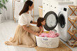 © Pixel-Shot - Young woman and her daughter setting up washing machine with dirty clothes in laundry room