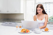 © WavebreakMediaMicro - Woman typing on laptop at modern kitchen island with pancakes topped with strawberries eggs mug
