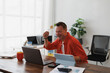 © Tj - Happy businessman raising his fist while celebrating success working from home office with laptop and tablet, he is laughing looking at the screen