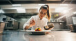 © Milan - Female chef plating a gourmet dish in a professional kitchen. Young cook preparing a meal with precision and care.