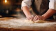 © Matthew - A baker skillfully kneads dough on a wooden table, with flour dusting the air in a cozy kitchen setting
