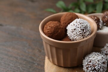 Wall Mural - Delicious homemade candies with cocoa powder and coconut flakes in bowl on wooden table, closeup. Space for text