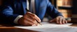 © Bohdana - The man in a suit signing a legal document in an elegant office setting.