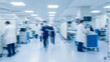 © birulaut - Blurred hospital interior with medical staff and equipment in a bright environment, featuring clean walls, sterile design, and a professional healthcare atmosphere.