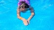 © Nastya Berry - A young girl with dark hair swims gracefully underwater in a vibrant blue pool, showcasing her swimming technique.