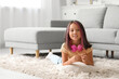 © Pixel-Shot - Cute little Asian girl with headphones lying on carpet in living room