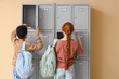 © Pixel-Shot - Teenage students opening locker on beige background, back view