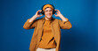 © BuyOutFelix04/peopleimages.com - Studio, dancing and man with headphones, music or listening to audio with tech, streaming or online. Blue background, space and person with smile for playlist, rhythm and happy for song on radio