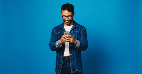 Reading, phone and glasses with man in studio for social media, communication and blog post. Online news feed, text message and networking chat with person on blue background for mockup space and app