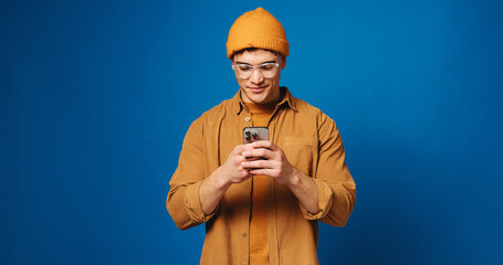 Phone, glasses and scroll with man in studio for social media, networking and connection. Mockup space, text message and search with person on blue background for contact, typing or communication app