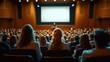 © Aleksandra - audience seated in a large auditorium attentively watching a speaker on stage with a blank screen behind