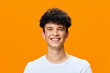 © SHOTPRIME STUDIO - smiling young man with curly dark hair wearing a white t-shirt, joyful expression, bright orange background, casual positive atmosphere, diverse ethnicity