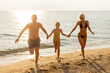 © BGStock72 - Happy family enjoys a sunny day at the beach holding hands and playing