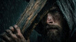 © sticker2you - Man with hood holds large wooden cross in rainstorm, raindrops on his face