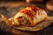 © halawiah - Golden, flaky pastry filled with savory meat filling on crinkled paper, wood background
