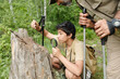 © pressmaster - Middle aged man and boy exploring nature together, boy using magnifying glass to examine tree stump while man observing, both holding trekking poles in forest setting