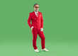 © Studio Romantic - Studio portrait of funny man in Christmas costume. Full length shot of man in stylish red suit, tie, white gloves and cool sunglasses standing on green colour studio background