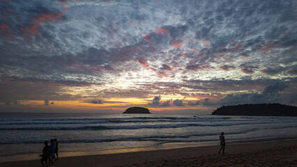 Wall Mural - Island Glow at Kata Beach Phuket. The last rays of sunshine illuminate the clouds with vibrant colors, blending seamlessly with the turquoise waters, a perfect moment of peace and wonder.